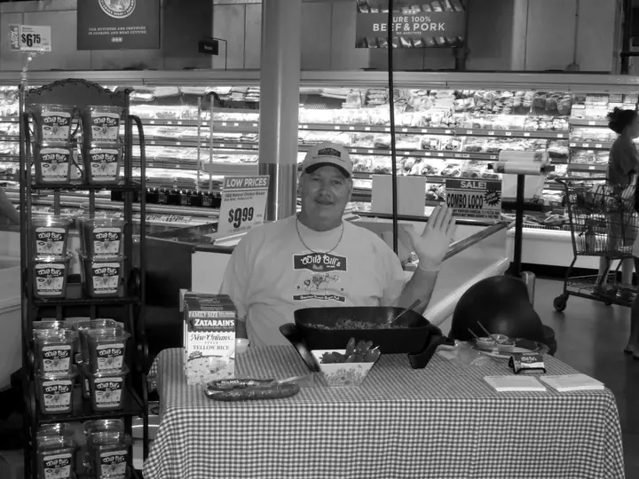 Bill Ramsey waving from his Wild Bill's Rib Rub tasting table in a grocery store