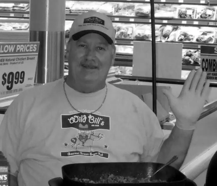 Bill Ramsey smiling and waving, wearing his Wild Bill's Rib Rub cap and shirt